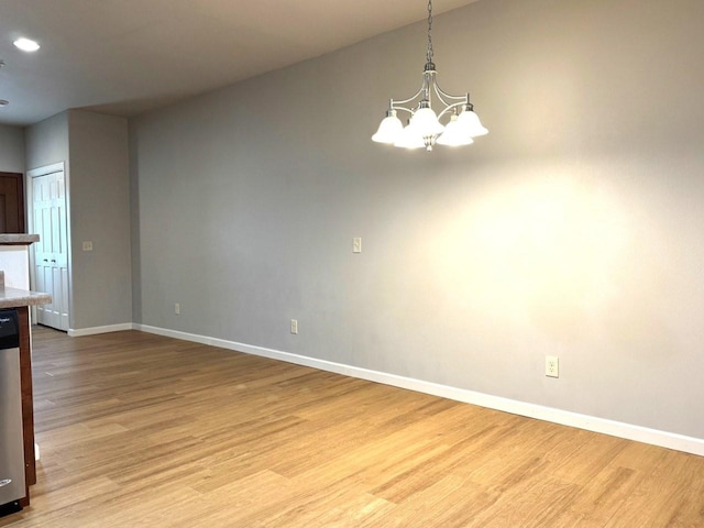 unfurnished dining area featuring an inviting chandelier, baseboards, and light wood finished floors