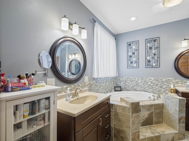 bathroom featuring two vanities, a garden tub, and a sink