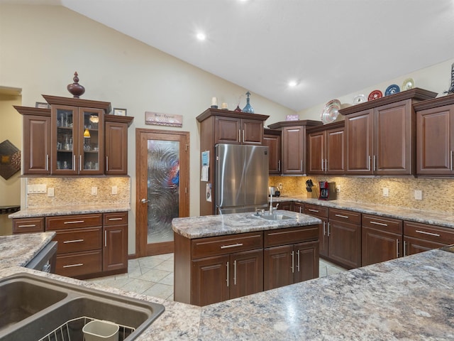 kitchen featuring tasteful backsplash, vaulted ceiling, freestanding refrigerator, light tile patterned flooring, and a sink