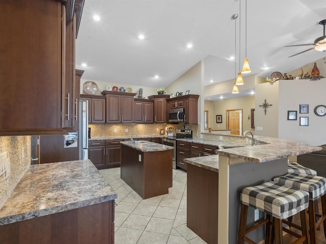 kitchen featuring a ceiling fan, a center island with sink, a peninsula, a sink, and stainless steel appliances