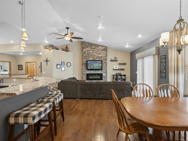 dining room featuring dark wood-style floors, ceiling fan with notable chandelier, a fireplace, and lofted ceiling