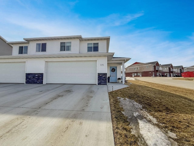 view of front of house featuring a residential view, stone siding, concrete driveway, and an attached garage