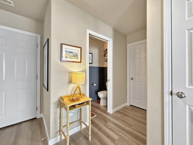 hallway with light wood finished floors, visible vents, and baseboards