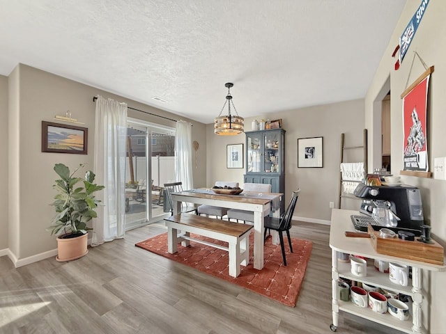 dining room with visible vents, a textured ceiling, wood finished floors, baseboards, and a chandelier