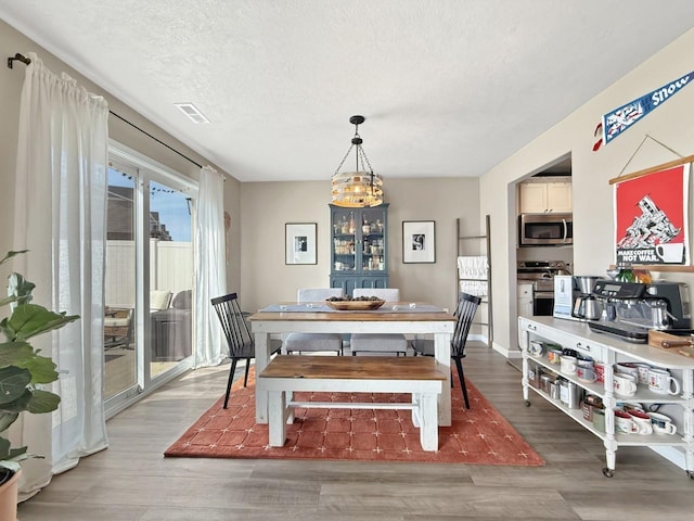 dining room with light wood finished floors, visible vents, baseboards, a chandelier, and a textured ceiling