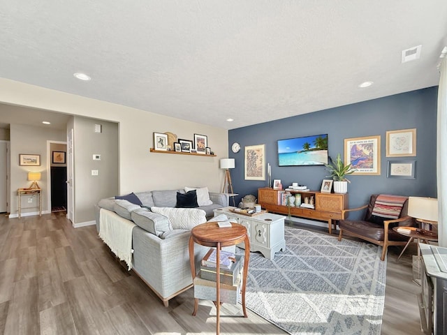 living room with wood finished floors, visible vents, baseboards, recessed lighting, and a textured ceiling