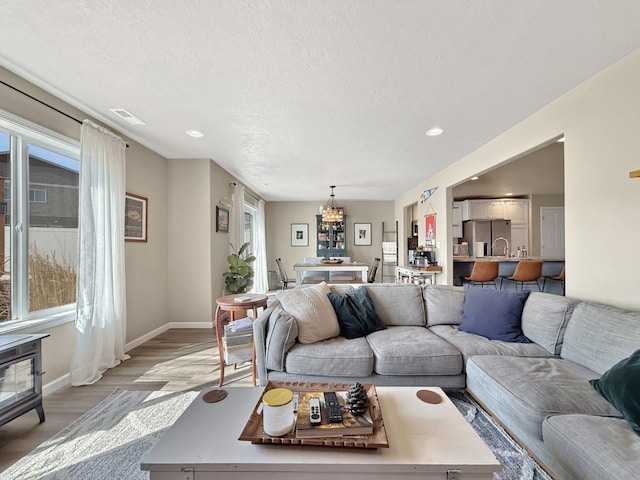 living room with an inviting chandelier, baseboards, light wood finished floors, and a textured ceiling