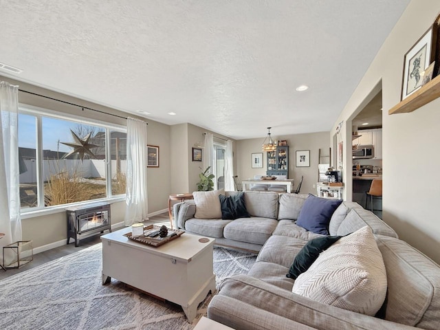 living area with visible vents, a notable chandelier, a textured ceiling, baseboards, and a wood stove