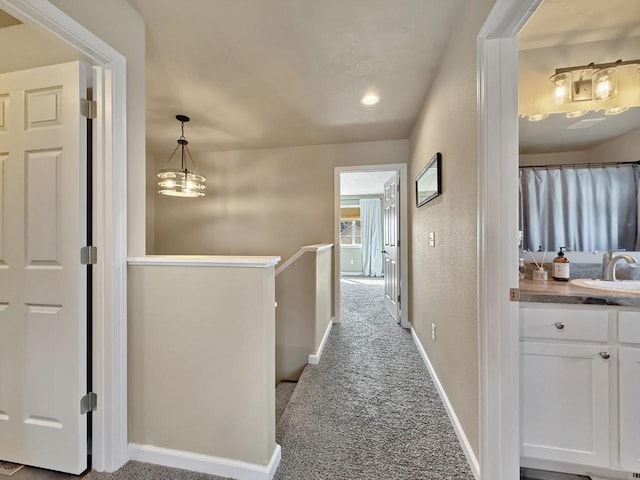 corridor featuring a sink, baseboards, carpet floors, and an upstairs landing