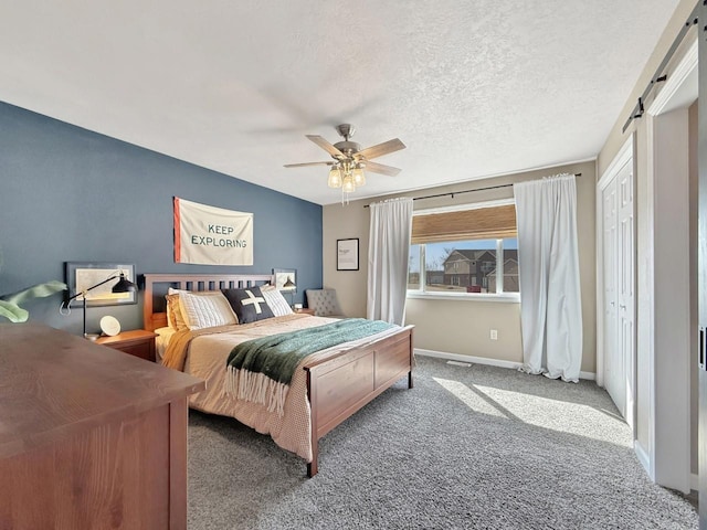 bedroom with baseboards, a barn door, carpet floors, a textured ceiling, and a ceiling fan