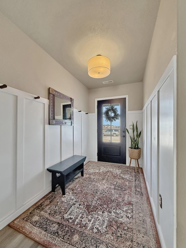 foyer entrance with a decorative wall, visible vents, and wood finished floors