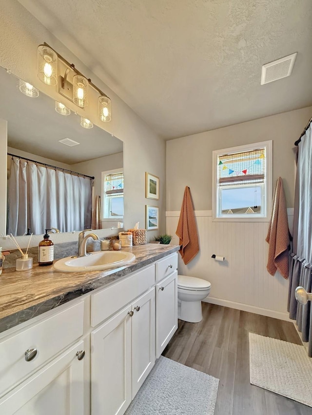 full bathroom featuring a wainscoted wall, visible vents, toilet, wood finished floors, and vanity