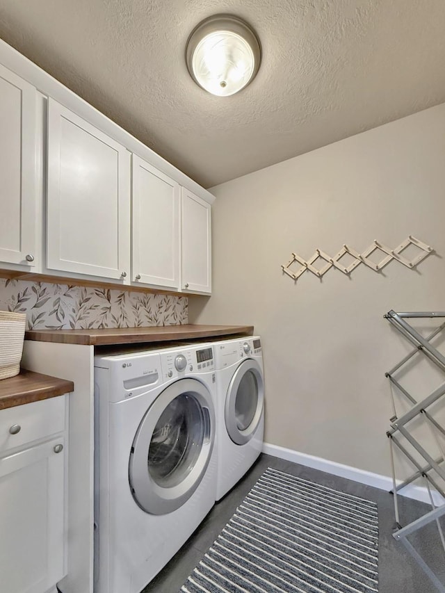 laundry area with baseboards, cabinet space, a textured ceiling, and washer and clothes dryer