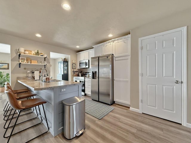 kitchen featuring light wood-style flooring, a kitchen breakfast bar, white cabinetry, stainless steel appliances, and a peninsula