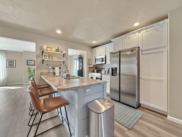 kitchen with a breakfast bar, light wood-style flooring, stainless steel appliances, light countertops, and white cabinets