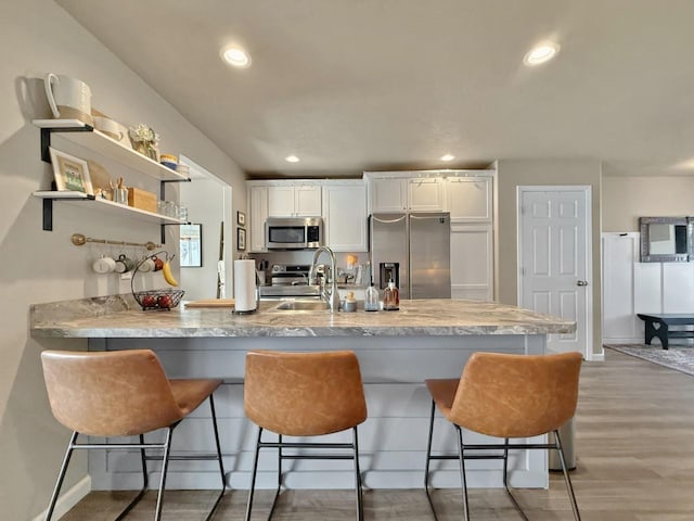 kitchen with a breakfast bar area, a peninsula, a sink, stainless steel appliances, and white cabinetry