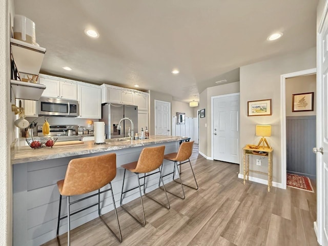 kitchen featuring light stone counters, light wood finished floors, a breakfast bar, stainless steel appliances, and white cabinetry