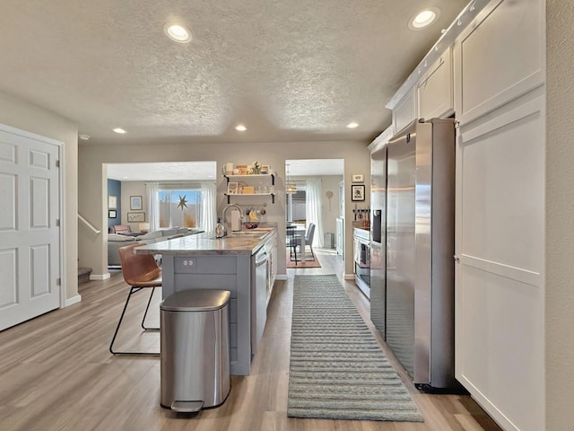 kitchen with a breakfast bar area, light wood-style flooring, appliances with stainless steel finishes, a textured ceiling, and a sink