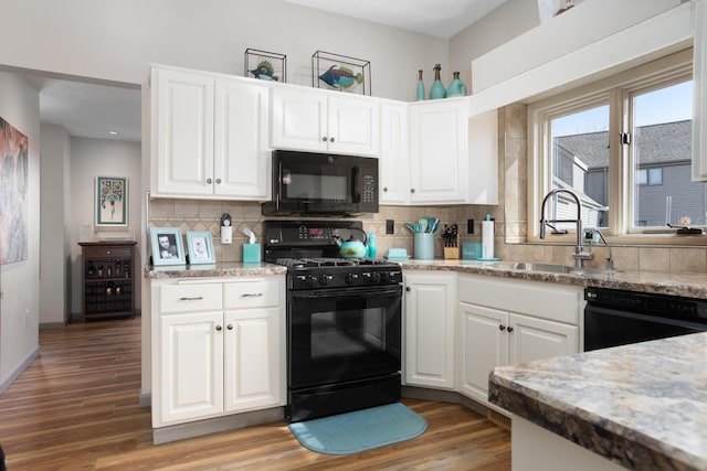 kitchen with black appliances, light wood-type flooring, backsplash, and a sink