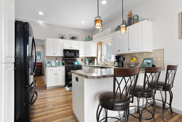 kitchen with a peninsula, a sink, black appliances, light wood-style floors, and white cabinetry