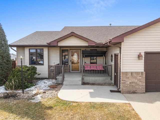 view of front of property with a garage, covered porch, roof with shingles, and brick siding