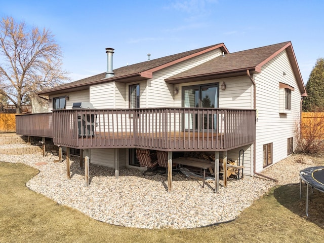 back of house featuring a deck, a trampoline, and roof with shingles