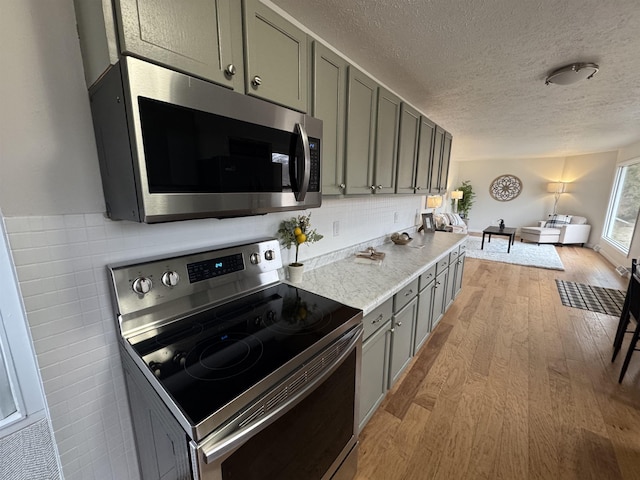 kitchen featuring backsplash, gray cabinets, appliances with stainless steel finishes, light wood-style floors, and a textured ceiling