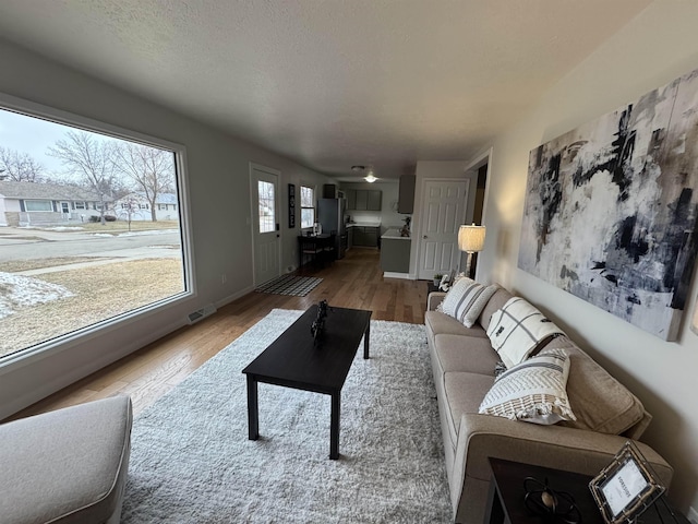 living area with visible vents, baseboards, a textured ceiling, and wood finished floors