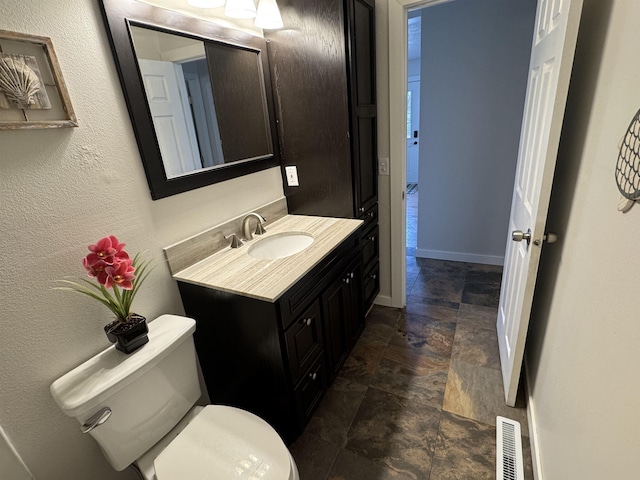 half bathroom with vanity, baseboards, visible vents, stone finish floor, and toilet