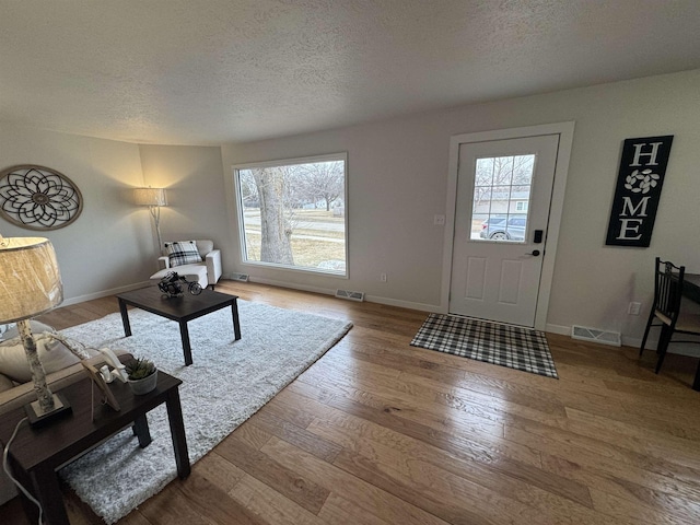 living area featuring a wealth of natural light, visible vents, baseboards, and wood finished floors