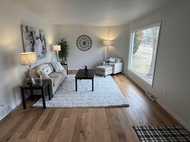 living room featuring visible vents, a textured ceiling, baseboards, and wood-type flooring