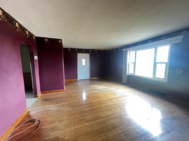 unfurnished room featuring arched walkways, baseboards, and wood finished floors