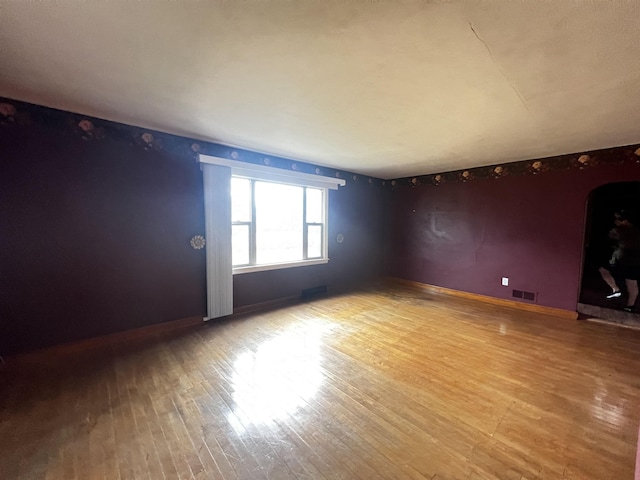 spare room with baseboards, visible vents, light wood-style floors, and arched walkways