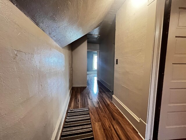 corridor with a textured ceiling, baseboards, wood finished floors, lofted ceiling, and a textured wall