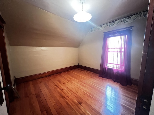 additional living space with baseboards, vaulted ceiling, and light wood-type flooring