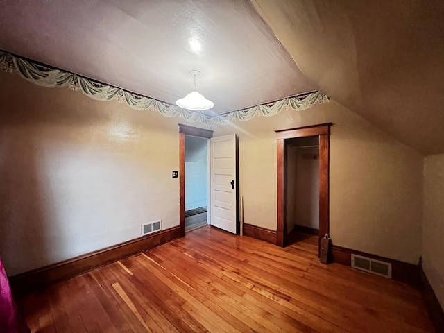 additional living space with hardwood / wood-style flooring, baseboards, vaulted ceiling, and visible vents