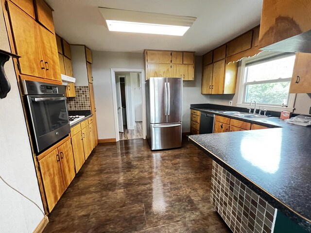 kitchen with dark countertops, tasteful backsplash, appliances with stainless steel finishes, under cabinet range hood, and a sink