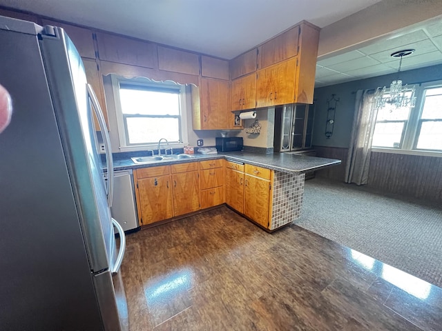 kitchen with an inviting chandelier, a sink, dark countertops, appliances with stainless steel finishes, and brown cabinets