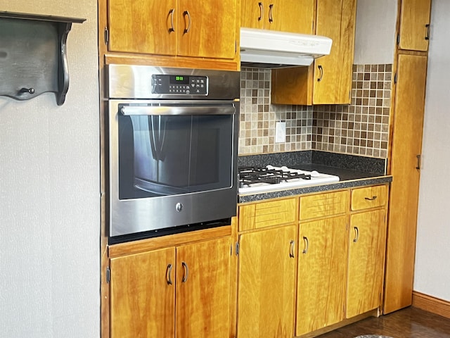 kitchen with decorative backsplash, white gas cooktop, oven, dark countertops, and under cabinet range hood