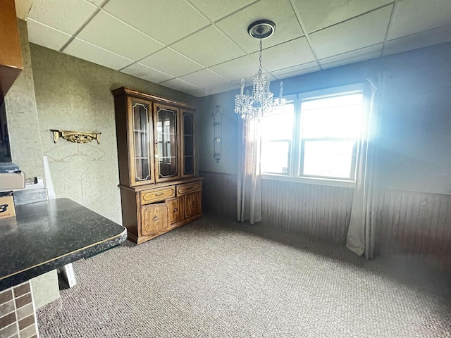 unfurnished dining area with a drop ceiling, carpet flooring, and a chandelier