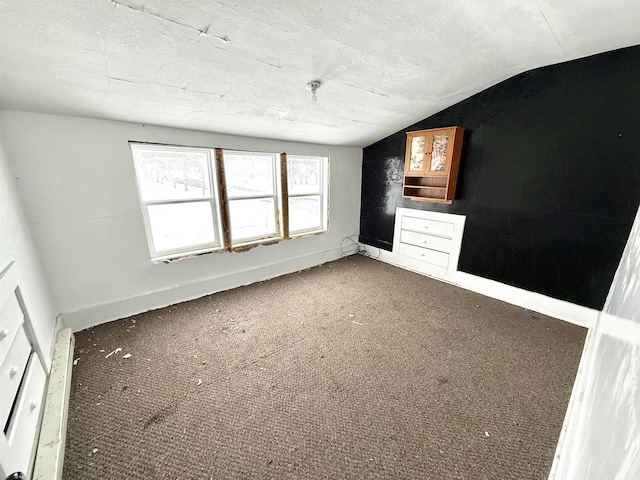 empty room with baseboards, lofted ceiling, carpet, and a textured ceiling