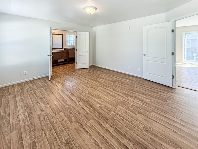 unfurnished bedroom with ensuite bathroom, baseboards, and light wood-style floors