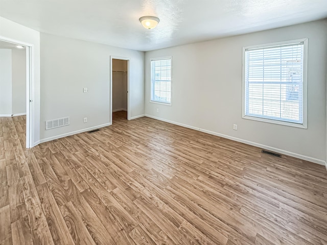 unfurnished bedroom featuring baseboards, light wood-style flooring, visible vents, and a spacious closet