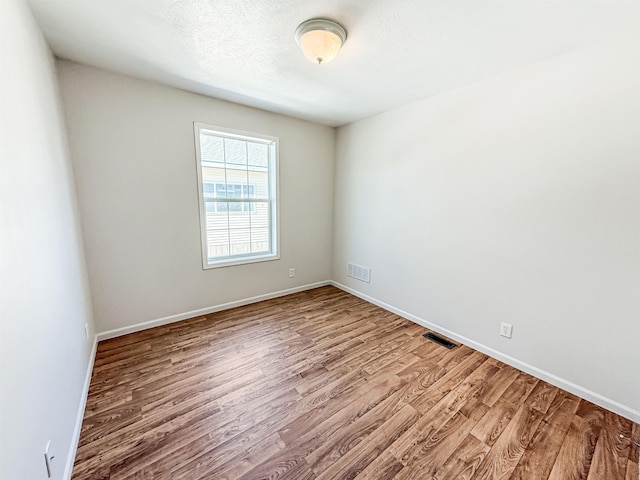 spare room featuring baseboards, a textured ceiling, visible vents, and wood finished floors