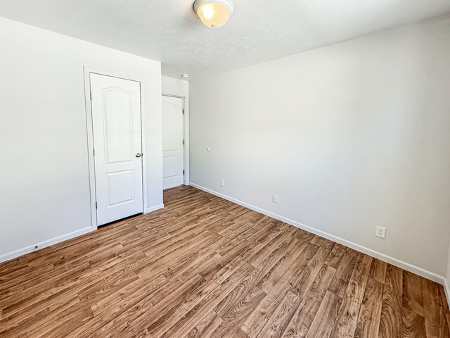 spare room featuring baseboards, light wood-style floors, and a textured ceiling