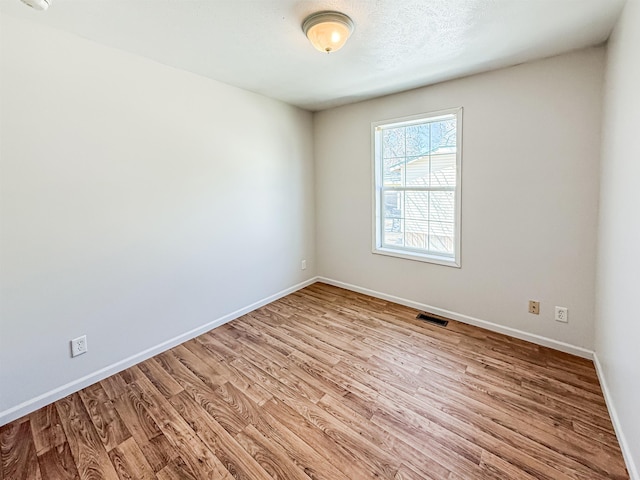 unfurnished room with a textured ceiling, baseboards, light wood finished floors, and visible vents