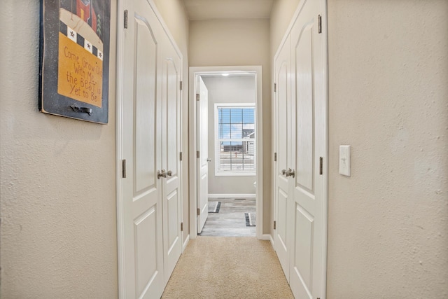 hallway with a textured wall, baseboards, and carpet