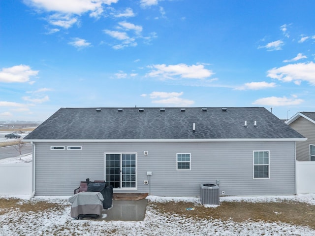 snow covered property featuring roof with shingles, fence, and central air condition unit