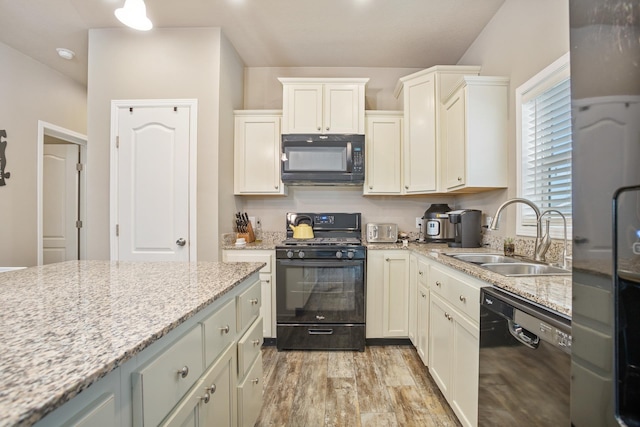 kitchen with light wood-type flooring, light stone counters, white cabinetry, black appliances, and a sink