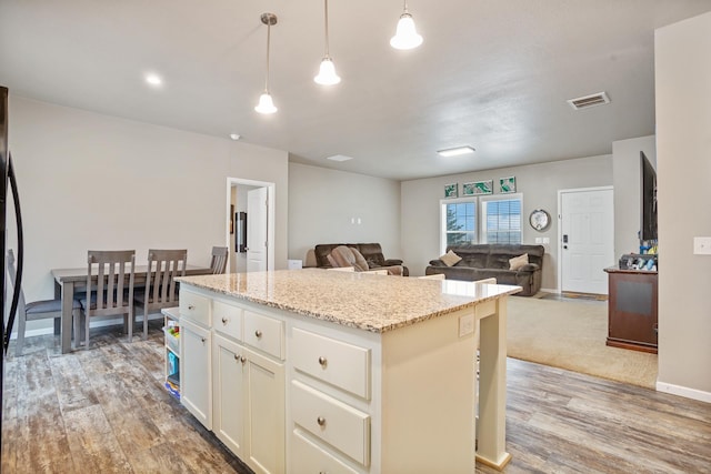 kitchen with light stone countertops, visible vents, a kitchen island, hanging light fixtures, and light wood finished floors